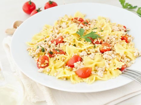 farfalle pasta with tomatoes, chiken meat, parsley on white stone background, low-calorie diet, the side view
