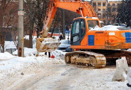 A large crawler excavator clears the street of packed snow from a city road. Copy space.