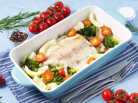 Fish cod baked in blue oven with a vegetables - broccoli, tomatoes. Healthy diet food. Blue stone background, side view.