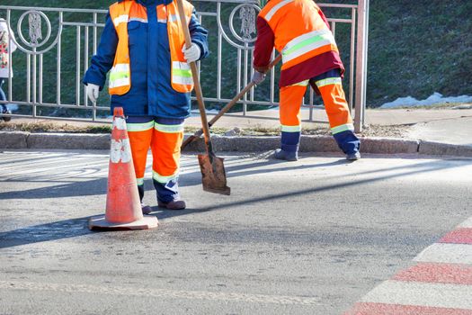 Wipers in bright orange reflective uniforms sweep the street and remove debris from the driveway and fence from orange traffic cones.