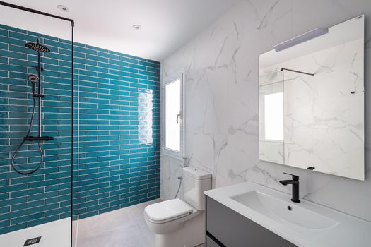 Decorated with dark aquamarine and white colors. Modern tiled bathroom with shower zone, new sink and toilets