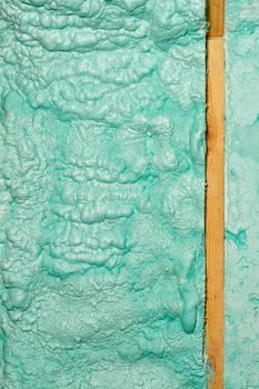 Texture and background of a wall made of ecological light green construction foam, laid in parallel rows near a wooden beam. Vertical image, close-up, high resolution.