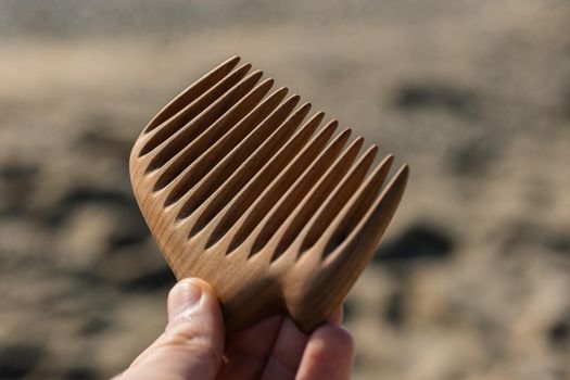 Handmade wooden comb for hair care in man hand.