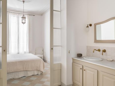 Bright bathroom interior with view to bedroom. Cozy bed with beige linen. Retro and vintage style.