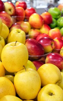 Bright yellow apples of the Golden variety, as well as red and green apples in a blur, lie on the counter and are sold in the bazaar, vertical image, close-up, copy space.