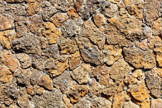 Texture of a rough masonry wall made of old weathered orange shell rock, illuminated by sunbeams with harsh shadows.