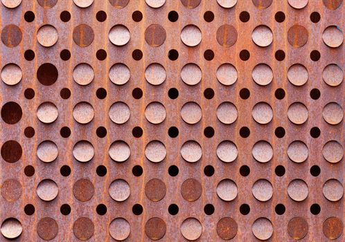 Old metal sheet with symmetrical round holes and rust texture, industrial decor in grunge style.