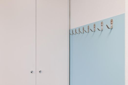 Metal hooks on light blue wall near white wardrobe in modern office. Minimalist style design