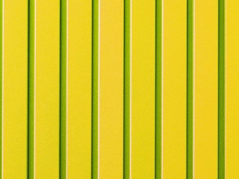 Yellow metal fence made of corrugated steel sheet with vertical rails. Corrugated yellow with light green stripes iron sheet close up background.