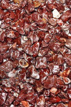 Beautiful texture of red wet granite in the form of fine gravel in polished pieces, rounded and polished. Vertical color photography, close-up.