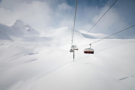 Chairlift in a ski resort, view from the funicular to the mountains and snow-covered fields for freeride skiing.