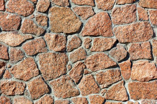 The texture wall of red granite and the background in the form of large blocks embedded in the wall in the light of warm sunlight, close-up, high resolution.