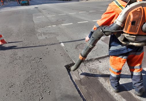 A worker with a blower removes dust from the repaired section of the road for subsequent better adhesion of bitumen to asphalt. Copy space.