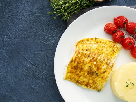 Fish cod baked in the oven with mashed potatoes, tomatoes, diet healthy food. Dark gray background, top view, copy space