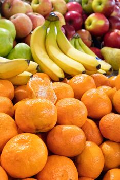 A heap of fresh ripe mandarin fruits, bananas and apples are on display on trays in the market and draw attention to the sale. Vertical image, selective focus.