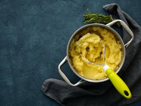 Mashed potatoes in bowl on a dark stone blue table, rosemary, napkin, top view