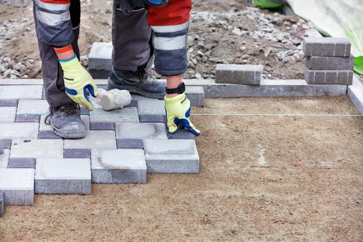 The hands of a bricklayer in protective gloves lay a pattern of paving slabs on a sandy base on the sidewalk under the level of a stretched thread, copy space, selective focus.