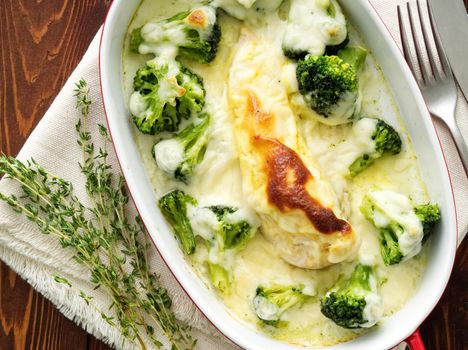 Chicken fillet baked with broccoli in bechamel sauce on a dark wooden table. Healthy food, clean eating, top view.