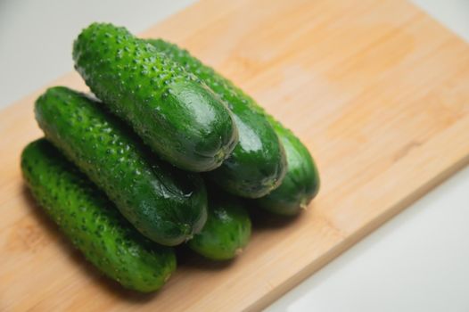 A pile of fresh small green cucumbers on a wooden cutting board on a white table.