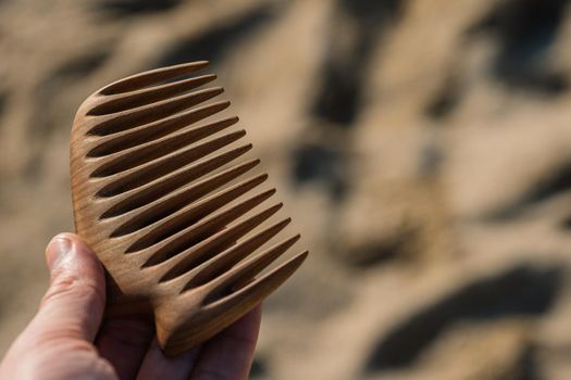 Handmade wooden comb for scalp massage and hair combing at sand background. Hair care concept.