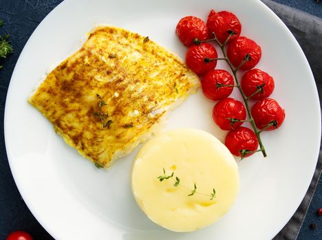 Fish cod baked in the oven with mashed potatoes, tomatoes, diet healthy food. Dark gray background, top view