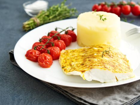 Fish cod baked in a oven with mashed potatoes, tomatoes, diet healthy food. Dark gray background, side view