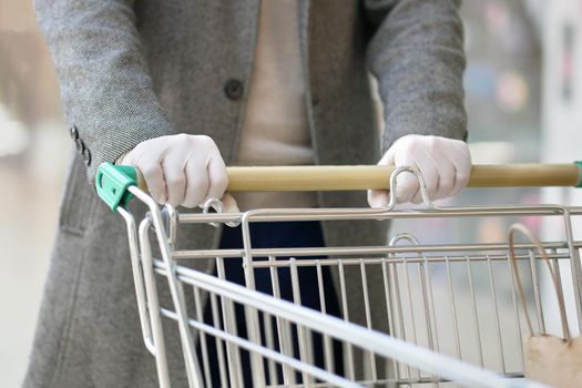 A man in medical gloves holds a grocery cart, close-up. No face visible