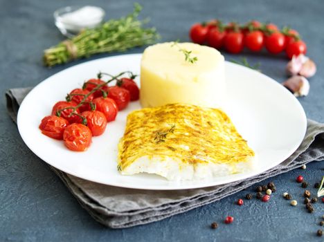 Fish cod baked in a oven with mashed potatoes, tomatoes, diet healthy food. Dark gray background, side view