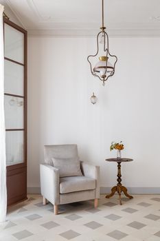 Living room interior with cozy armchair and side table near white wall. Retro style with vintage chandelier