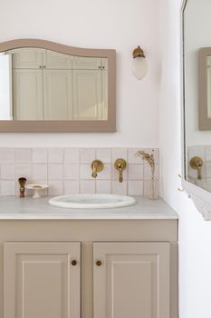 Bathroom decorated in beige color with sinks, golden faucets and vintage mirror. Interior of restroom in retro or classic style
