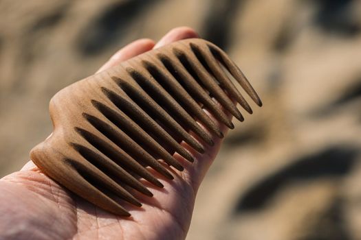 Wooden comb on a palm at sand background. Tool for scalp massage and aroma combing. Hair care concept