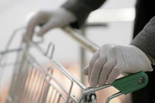 A man in medical gloves holds a grocery cart, close-up. No face visible