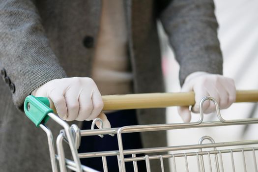 A man in medical gloves holds a grocery cart, close-up. No face visible