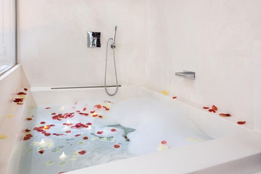 Rose petals put in bathtub for romantic bathroom atmosphere. Bubble bath arranged for honeymoon couple