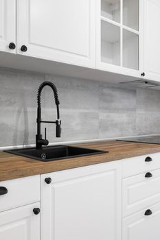 Simple and elegant kitchen with wooden countertop, white cupboards, drawers and black sink