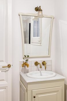 Bathroom decorated in beige color with small sink, bronze faucet and vintage mirror. Interior of retro or classic style