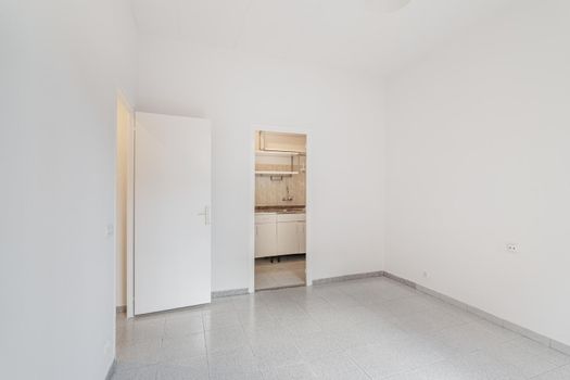 Empty white room connected with small kitchen. Typical apartment for rent in Barcelona