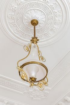 Vintage chandelier in the interior of white room with stucco molding on the ceiling.
