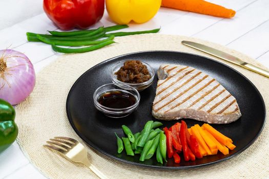 Grilled tuna steak on black plate with sauce, caramelized onion and fresh vegetables.