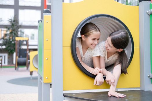 kids outdoors having fun on modern playground with new colorful equipment. sisterhood, friendship. two charming girls playing outdoors. sister, bffs, friends.