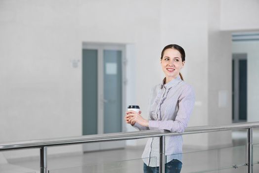 young attractive woman with a paper cup of coffee, rests on railing