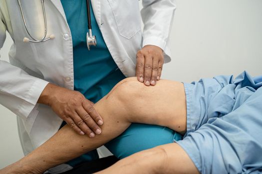 Asian doctor physiotherapist examining, massaging and treatment knee and leg of senior patient in orthopedist medical clinic nurse hospital.