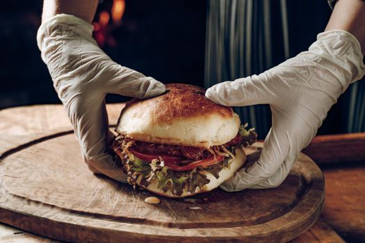 Gloved hands take a hamburer from a wooden tray. High quality photo