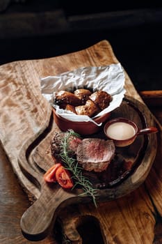 Juicy delicious steak with sauce and baked potatoes on a wooden surface. High quality photo