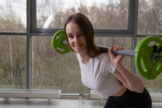 Her The in a girl hands with barbell smiles barbell strong female woman, from warehouse weights in gym and young one, holding cross. Sports determination women, sportswoman adult active