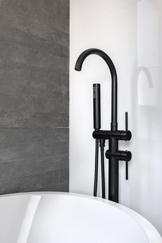 New black faucet and shower head against clean tiled white and gray wall of bathroom in modern apartment. Minimalist interior design.