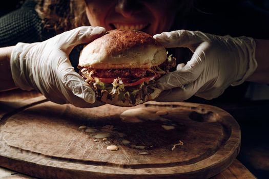 Gloved hands take a hamburer from a wooden tray. High quality photo