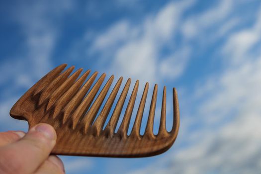 Handmade wooden comb for scalp massage and hair combing at blue sky background. Hair care concept