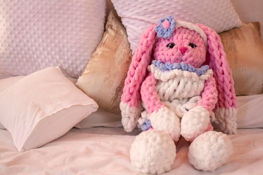 pink rabbit knitted toy sits on the sofa. Animal crochet. Amigurumi. Place for text.