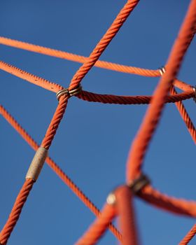 Abstract detail picture of climbing frame with red ropes and blue sky in playground